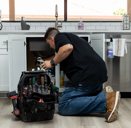 Meet the Team 33 Robert Bridge fixing under-sink plumbing with tool bag, Bridge Plumbing & HVAC repair.
