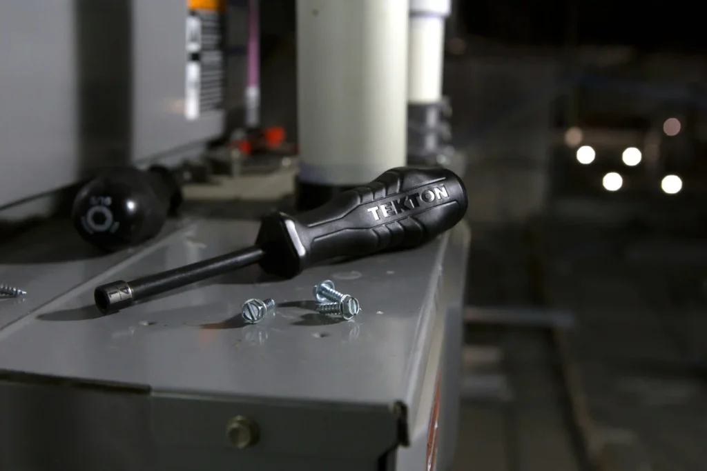 Black Tekton screwdriver and screws on top of HVAC equipment. HVAC Inspection