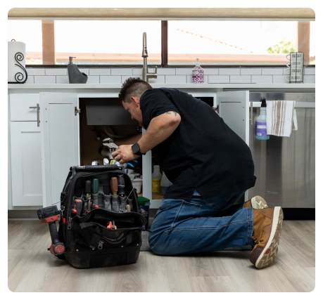 Special Offers 50 Robert Bridge kneeling under a kitchen sink with a tool bag beside him.