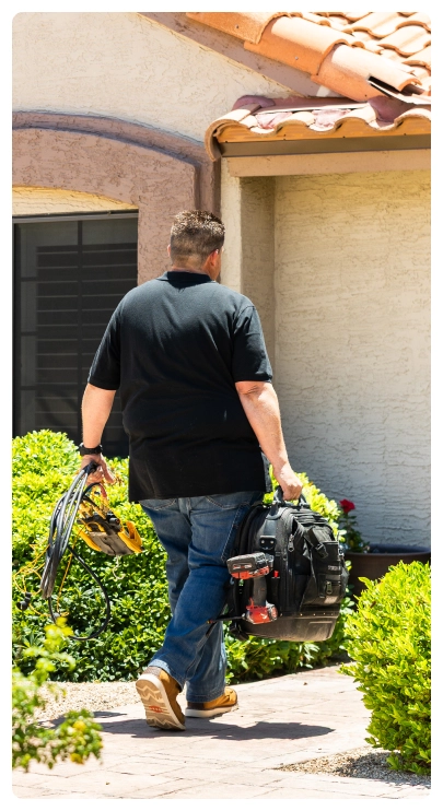 Furnace Repair 36 Robert Bridge walking toward a house carrying a tool bag and cables.